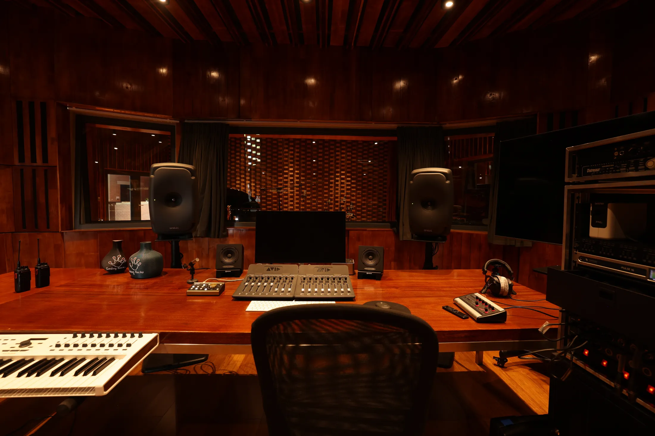 The control room: mixing console and reference monitors on a wooden desk, with the live room through the window