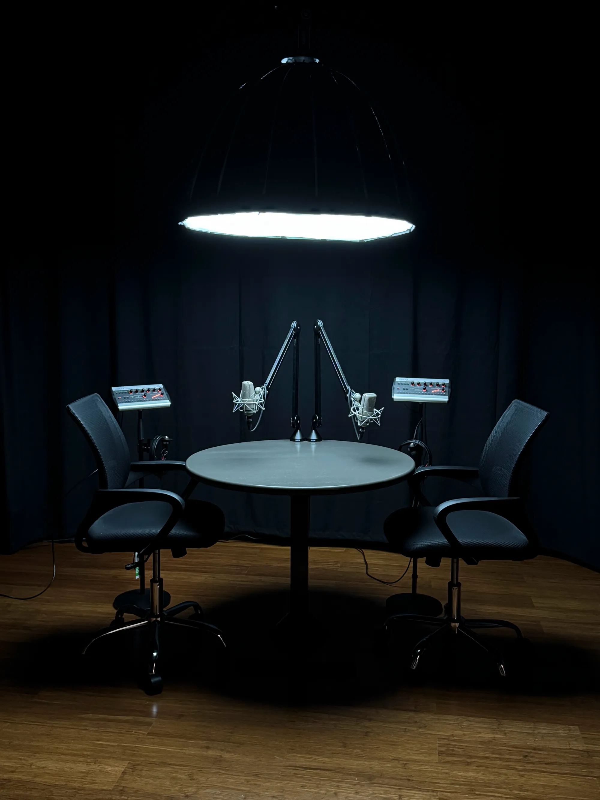 The podcast studio: two microphones face each other across a round table under a single hanging light